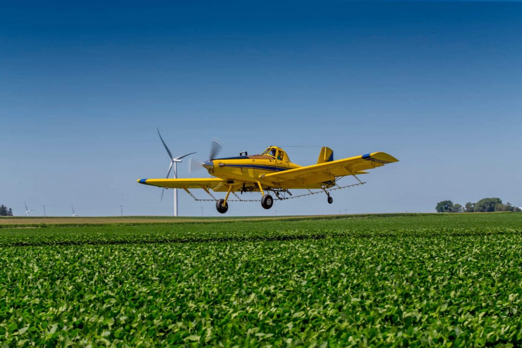 Crop duster plane spraying over vast farmland.
