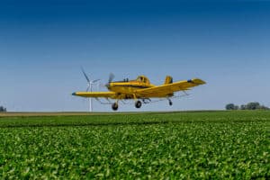 Crop duster plane spraying over vast farmland.