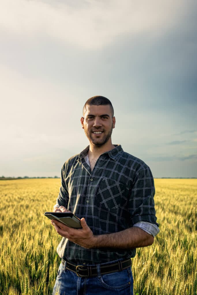 Farmer using a digital tablet with AgTech analytics in a traditional farmland setting.